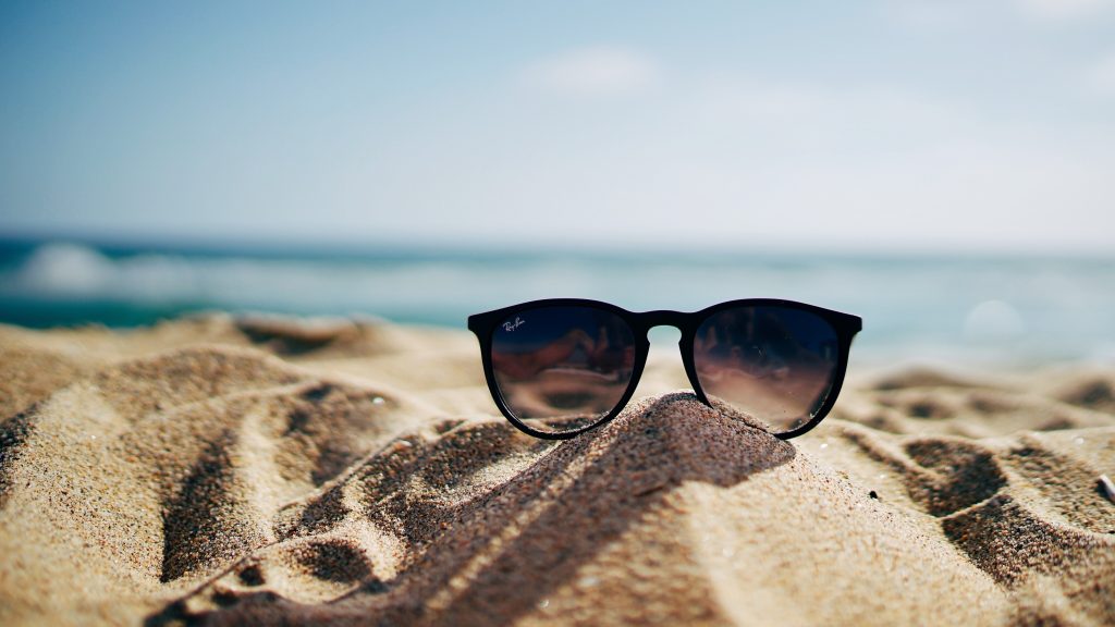 Sunglasses on sandy beach with ocean background.