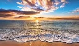 Sunset over ocean waves and sandy beach.