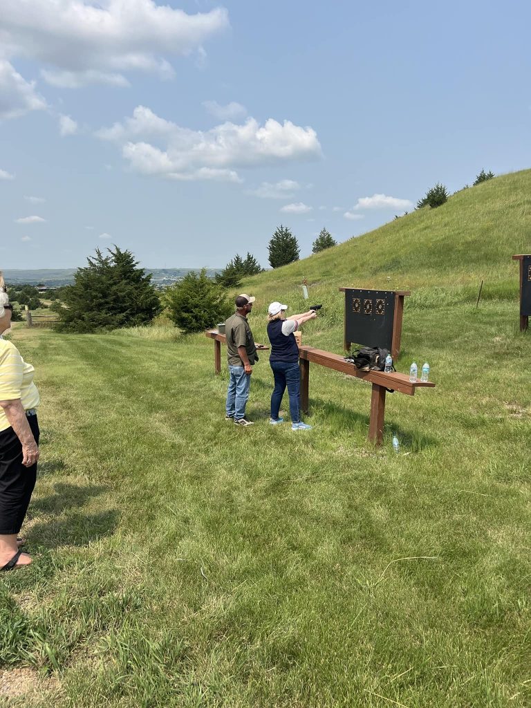 People target shooting outdoors on grassy hill.